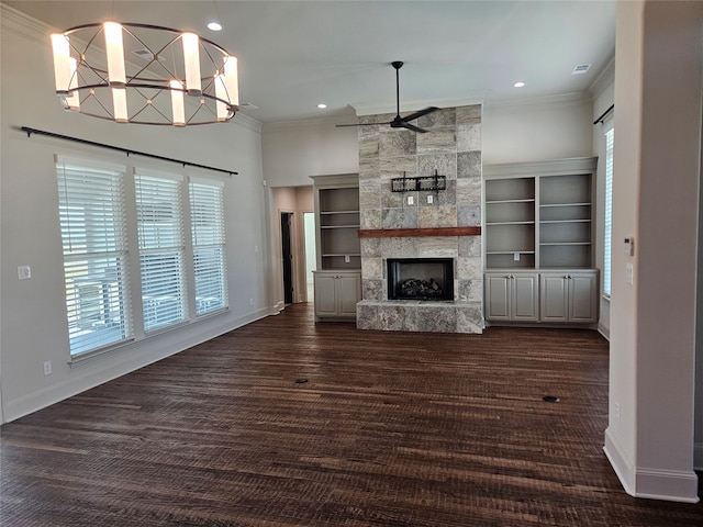 unfurnished living room featuring built in shelves, ornamental molding, a stone fireplace, dark wood-type flooring, and ceiling fan with notable chandelier