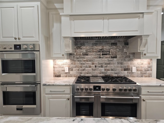 kitchen with light stone counters, white cabinets, stainless steel appliances, and backsplash