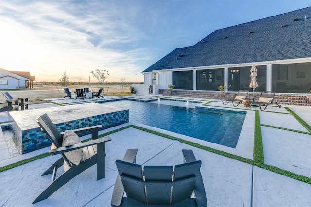 pool at dusk featuring a patio and pool water feature