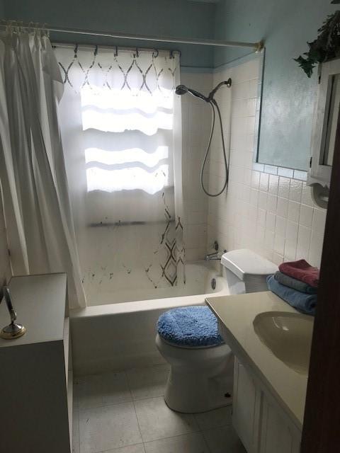 full bathroom with tile patterned flooring, vanity, shower / tub combo, tile walls, and toilet