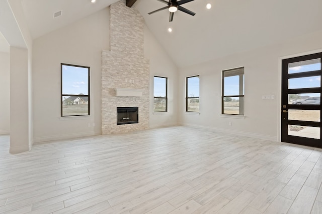 unfurnished living room with high vaulted ceiling, ceiling fan, a stone fireplace, light hardwood / wood-style flooring, and a healthy amount of sunlight