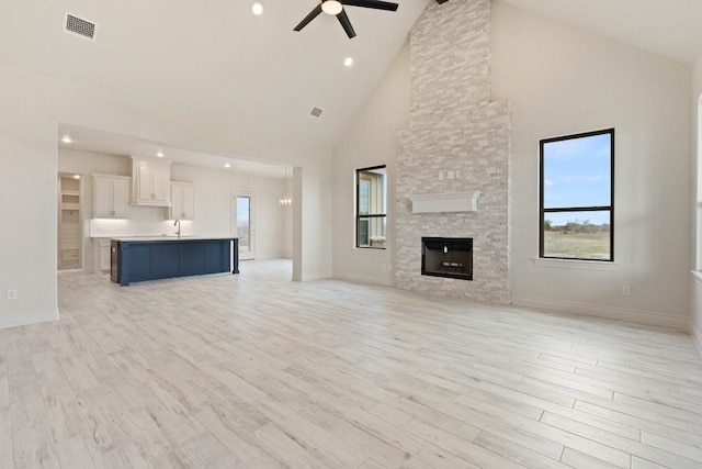 unfurnished living room with light hardwood / wood-style floors, a stone fireplace, ceiling fan, high vaulted ceiling, and sink