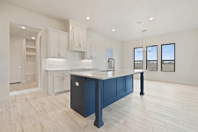 kitchen featuring an island with sink, hanging light fixtures, white cabinetry, and sink