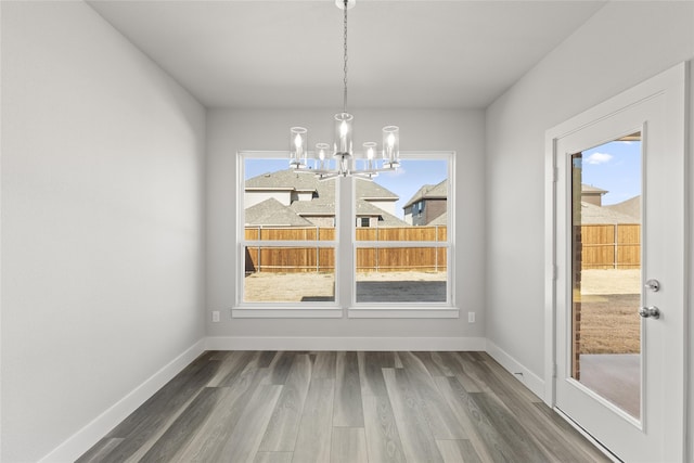 unfurnished dining area with wood-type flooring and a notable chandelier