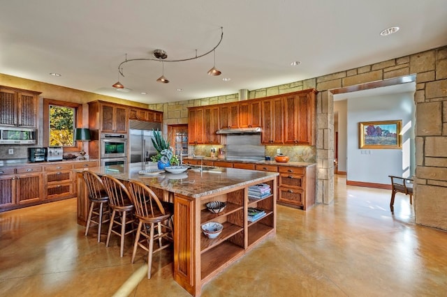 kitchen featuring decorative light fixtures, stainless steel appliances, dark stone countertops, a breakfast bar area, and a center island with sink