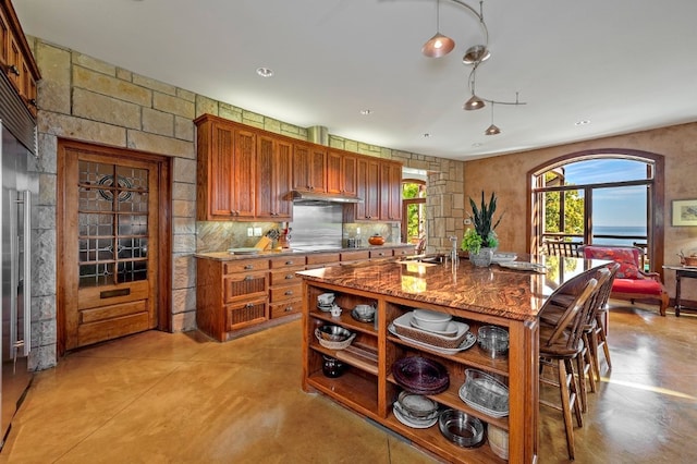 kitchen featuring stovetop, an island with sink, sink, built in refrigerator, and light stone counters