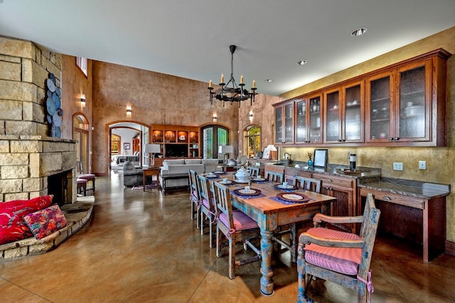 dining space featuring a fireplace, a towering ceiling, concrete flooring, and a chandelier