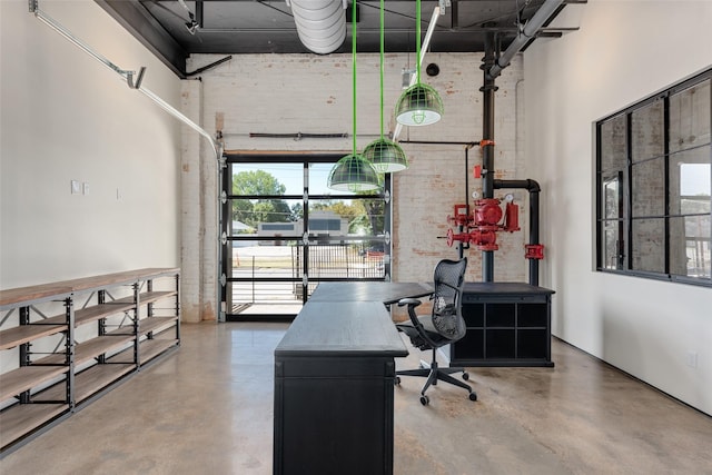 office space featuring concrete floors, brick wall, and a high ceiling