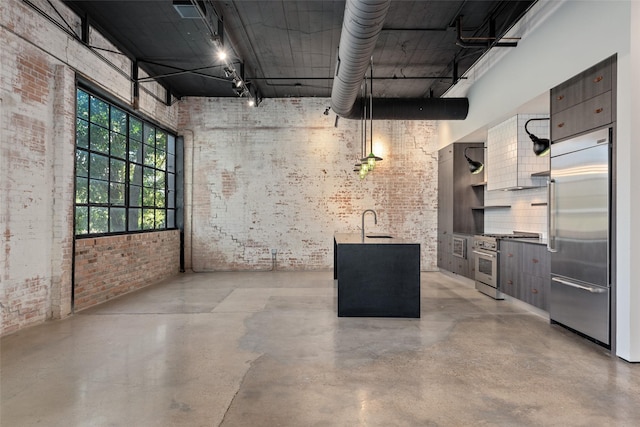 basement featuring sink, track lighting, stainless steel built in fridge, and brick wall