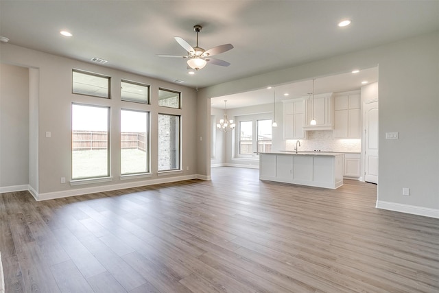 unfurnished living room featuring sink, ceiling fan with notable chandelier, and light wood-type flooring