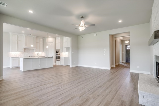 unfurnished living room with sink, a fireplace, ceiling fan, and light hardwood / wood-style floors