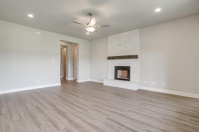 unfurnished living room featuring brick wall, a fireplace, ceiling fan, and light hardwood / wood-style floors