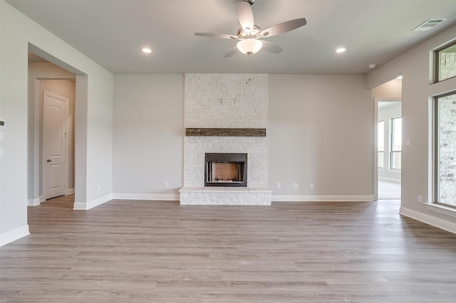 unfurnished living room with ceiling fan, a fireplace, and light hardwood / wood-style flooring