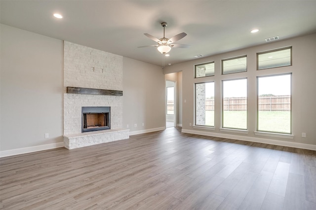 unfurnished living room with wood-type flooring, a stone fireplace, and ceiling fan