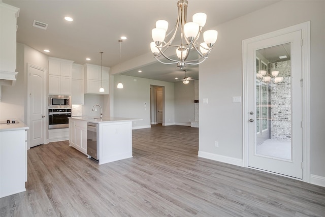 kitchen featuring stainless steel appliances, a center island with sink, white cabinets, hanging light fixtures, and light wood-type flooring