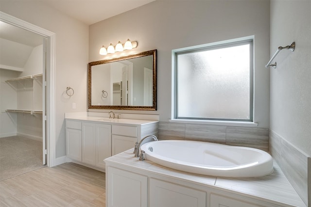 bathroom with tiled tub, vanity, and plenty of natural light