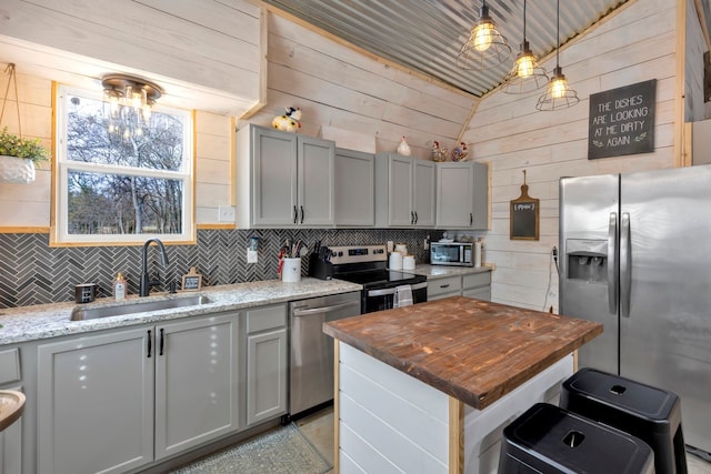 kitchen with lofted ceiling, light stone counters, stainless steel appliances, sink, and wood walls