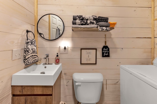 bathroom featuring washer / clothes dryer, vanity, wood walls, and toilet