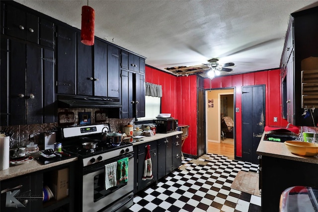 kitchen with under cabinet range hood, stainless steel range with gas cooktop, tile patterned floors, a ceiling fan, and light countertops