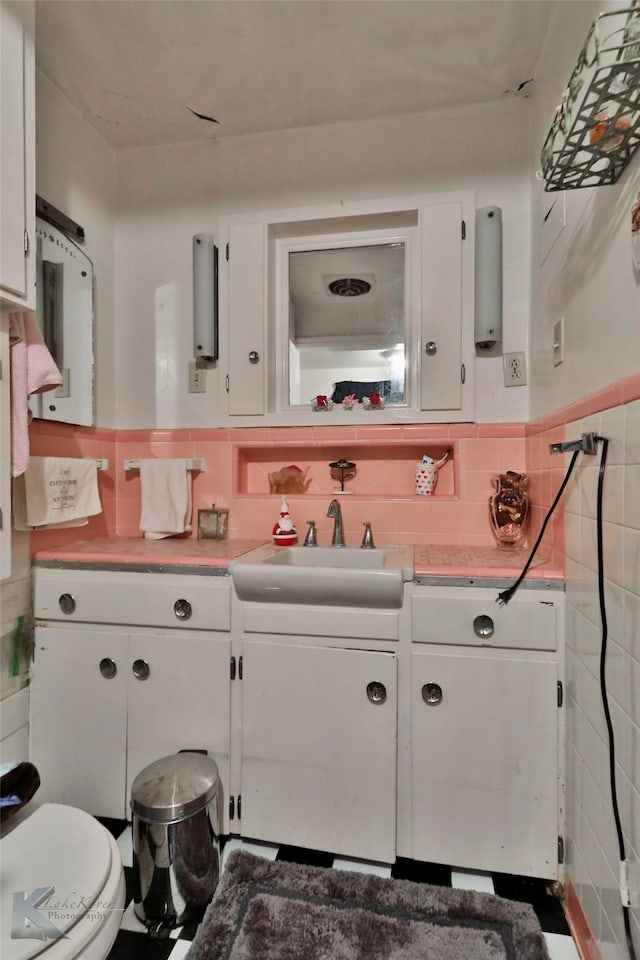 half bath with tile walls, wainscoting, toilet, and vanity