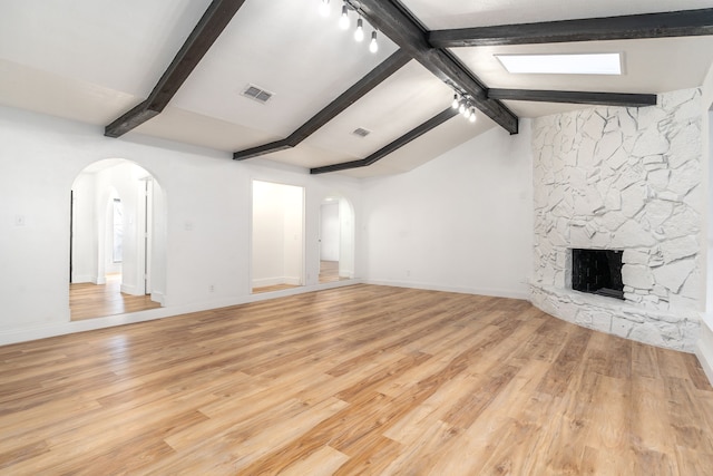 unfurnished living room featuring lofted ceiling with beams, a stone fireplace, and light hardwood / wood-style flooring