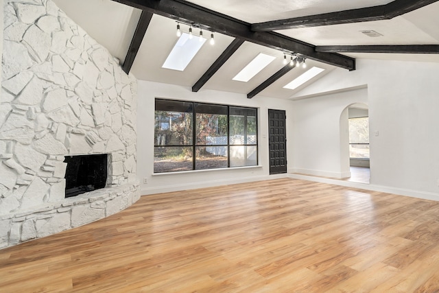 unfurnished living room with rail lighting, light hardwood / wood-style flooring, lofted ceiling with skylight, and a stone fireplace