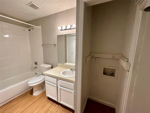 full bathroom featuring vanity, hardwood / wood-style flooring, tiled shower / bath combo, toilet, and a textured ceiling