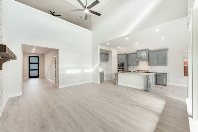 unfurnished living room featuring sink, ceiling fan, a fireplace, high vaulted ceiling, and light wood-type flooring