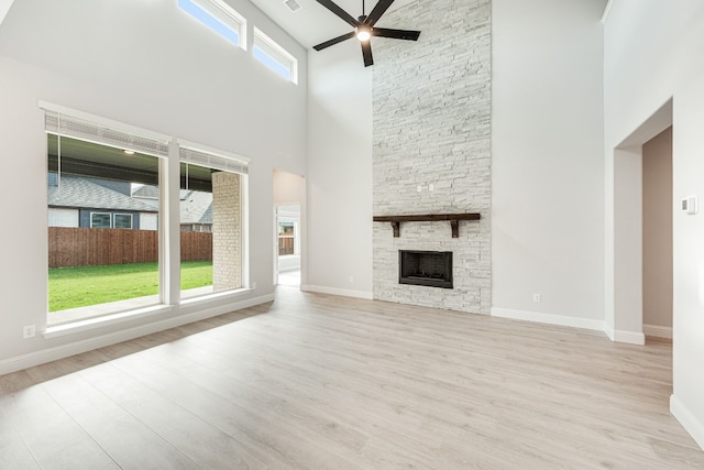 unfurnished living room featuring a towering ceiling, a stone fireplace, ceiling fan, and light wood-type flooring