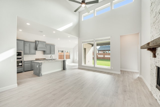 unfurnished living room with sink, ceiling fan, a towering ceiling, light hardwood / wood-style floors, and a fireplace