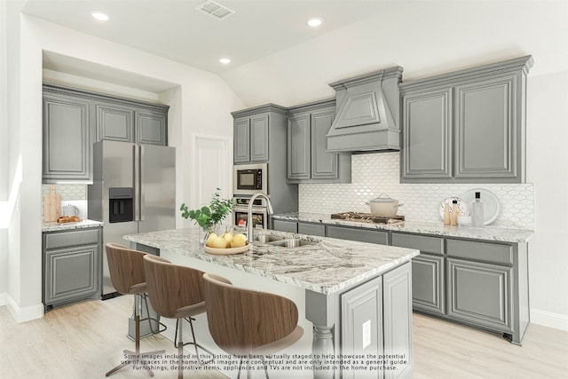 kitchen featuring backsplash, an island with sink, custom exhaust hood, and light wood-type flooring