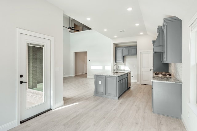 kitchen featuring gray cabinetry, backsplash, ceiling fan, a kitchen island with sink, and light hardwood / wood-style floors