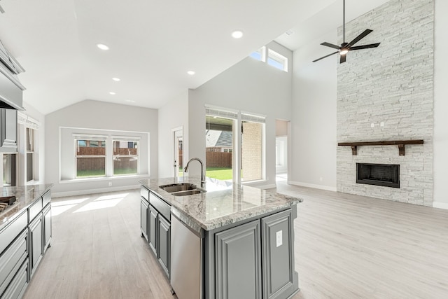 kitchen with a kitchen island with sink, ceiling fan, sink, a fireplace, and light wood-type flooring