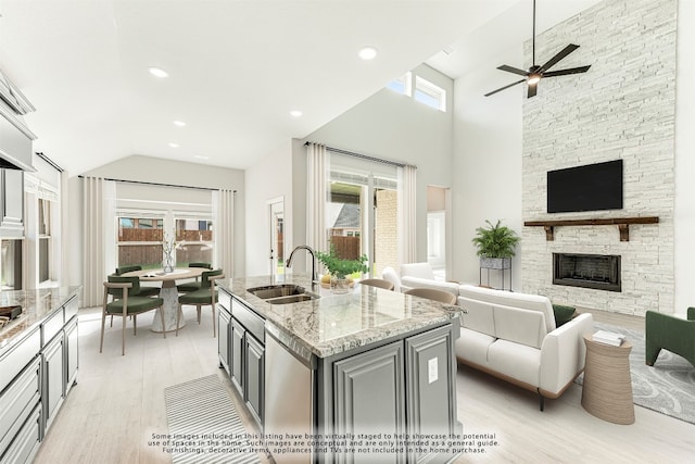 kitchen with light hardwood / wood-style floors, light stone countertops, ceiling fan, a stone fireplace, and sink