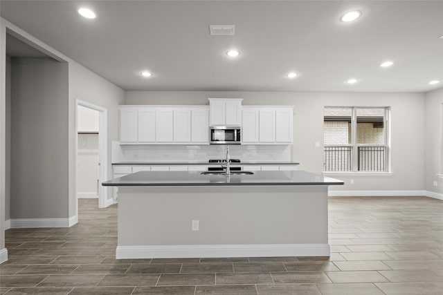 kitchen featuring white cabinets, sink, backsplash, tile floors, and an island with sink