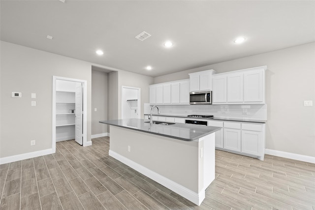 kitchen with backsplash, sink, a center island with sink, and white cabinetry