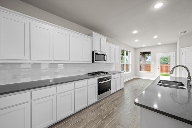 kitchen featuring appliances with stainless steel finishes, white cabinets, sink, backsplash, and dark stone counters