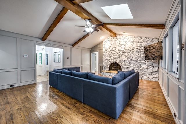 living room with hardwood / wood-style floors, ceiling fan, a fireplace, and vaulted ceiling with skylight