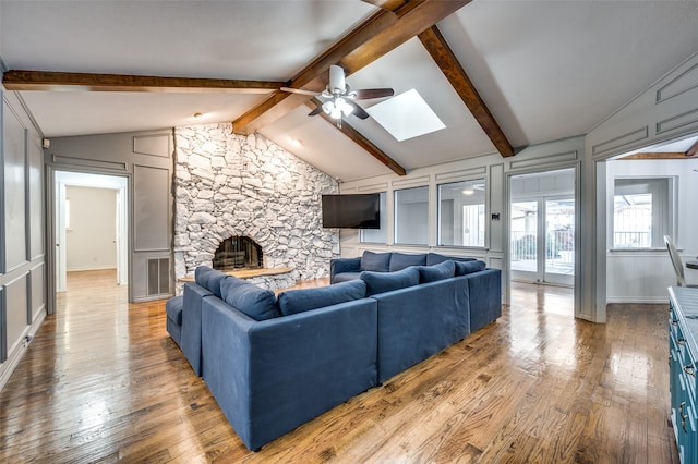 living room featuring a stone fireplace, ceiling fan, lofted ceiling with skylight, and wood-type flooring