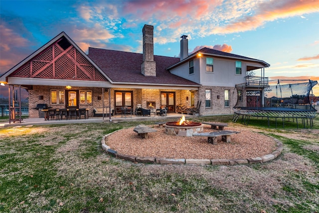 back house at dusk with a patio area, a trampoline, and an outdoor fire pit