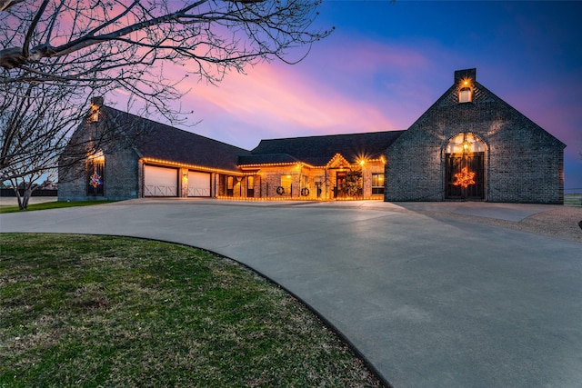 view of front of house with brick siding, a yard, a chimney, concrete driveway, and a garage