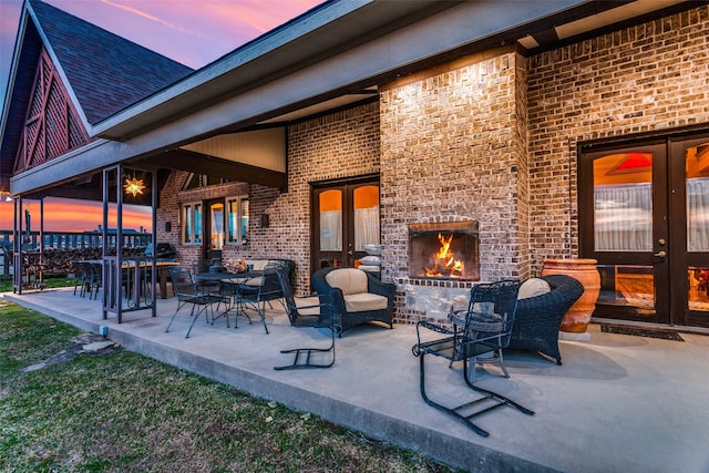 patio terrace at dusk featuring french doors and an outdoor brick fireplace