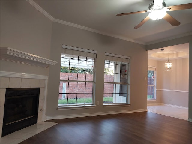 unfurnished living room with a wealth of natural light, a tile fireplace, ceiling fan with notable chandelier, and hardwood / wood-style floors