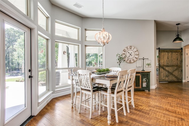 dining area with wood-type flooring, a notable chandelier, and a barn door