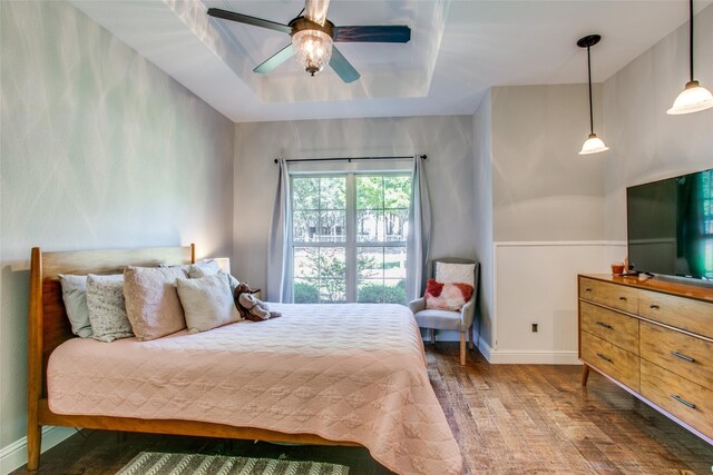 bedroom with ceiling fan, a tray ceiling, and dark hardwood / wood-style flooring