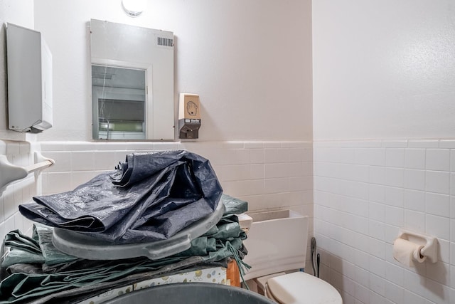 half bath with toilet, a wainscoted wall, and tile walls