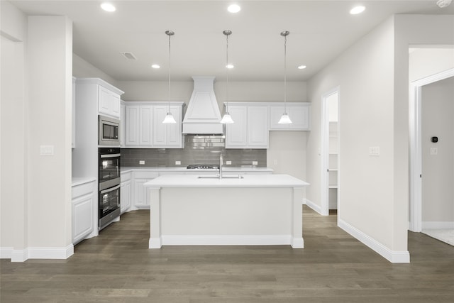 kitchen with decorative backsplash, custom range hood, appliances with stainless steel finishes, hardwood / wood-style flooring, and a center island with sink