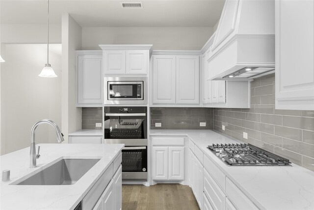 kitchen with sink, custom range hood, light wood-type flooring, stainless steel appliances, and white cabinets