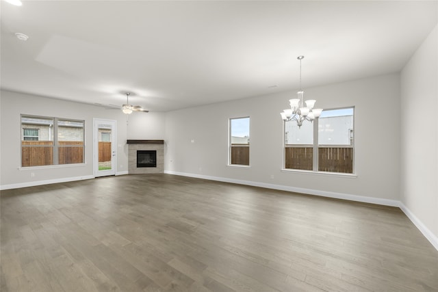 unfurnished living room with plenty of natural light, ceiling fan with notable chandelier, hardwood / wood-style flooring, and a tile fireplace