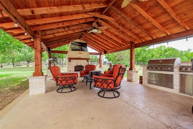 view of patio featuring grilling area, exterior kitchen, an outdoor stone fireplace, a gazebo, and ceiling fan